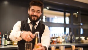 Un bartender preparando una bebida detrás de la barra, con varias botellas y vasos.
