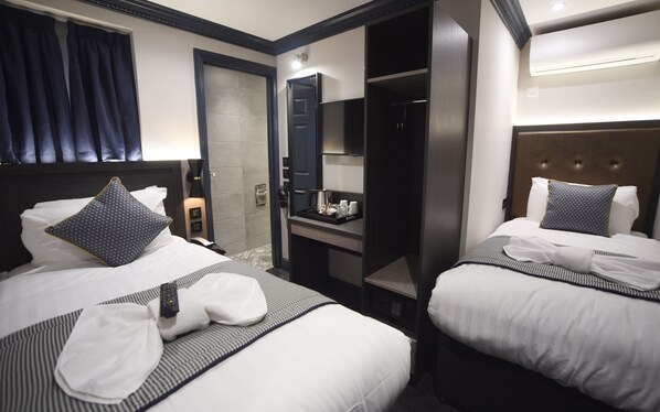 A hotel room with two beds, a minibar, a mirror, and a door leading to a bathroom. - The Pack And Carriage London (London)