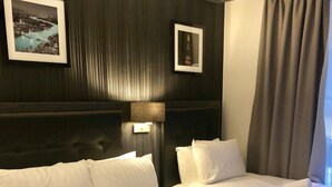 Habitación de hotel con dos camas, una mesita de noche, una lámpara y cuadros en la pared.