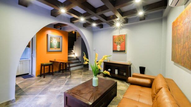 A living room with a brown leather sofa, a wooden coffee table with a vase of flowers, and a staircase leading to an upper level. - Le Petit Hanoi (Hanoi)