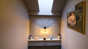 A room with a skylight, a brick wall, a shelf with decorative items, and a painting. - Le Petit Hanoi (Hanoi)