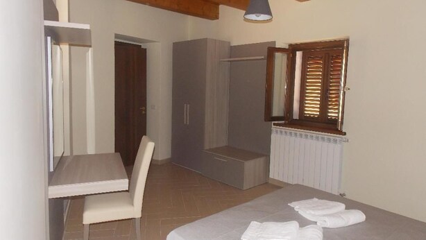 Un dormitorio con cama, una silla, armario, zona de ducha y ventana con persianas.