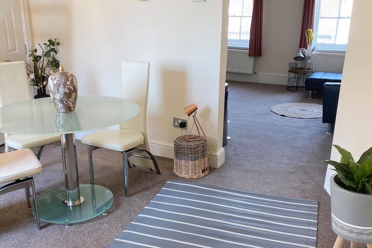A modern living room with a glass dining table, striped rug, and a potted plant.