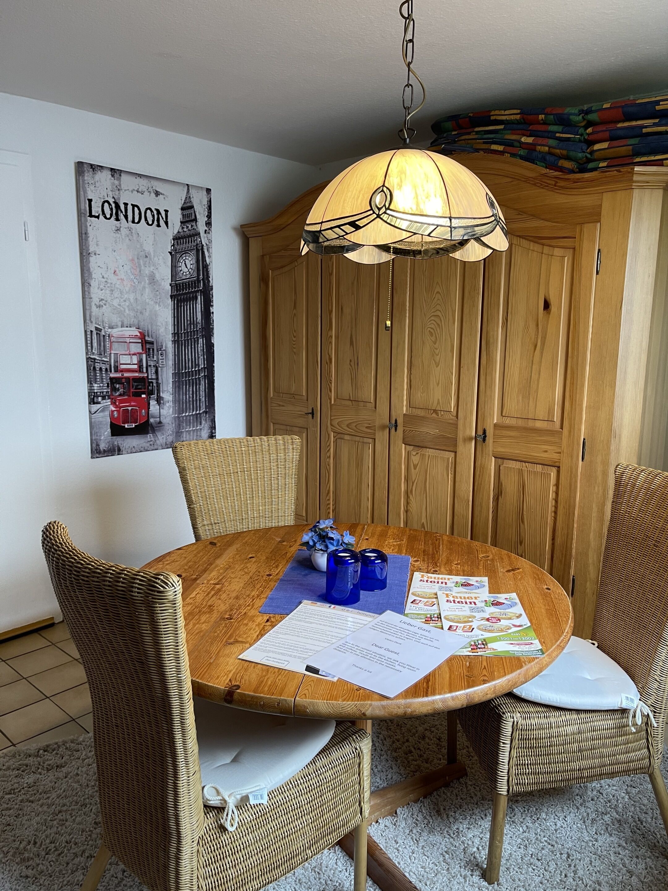 Ein runder Holztisch mit Korbstühlen, einer Pendelleuchte und einem Londoner Poster an der Wand.