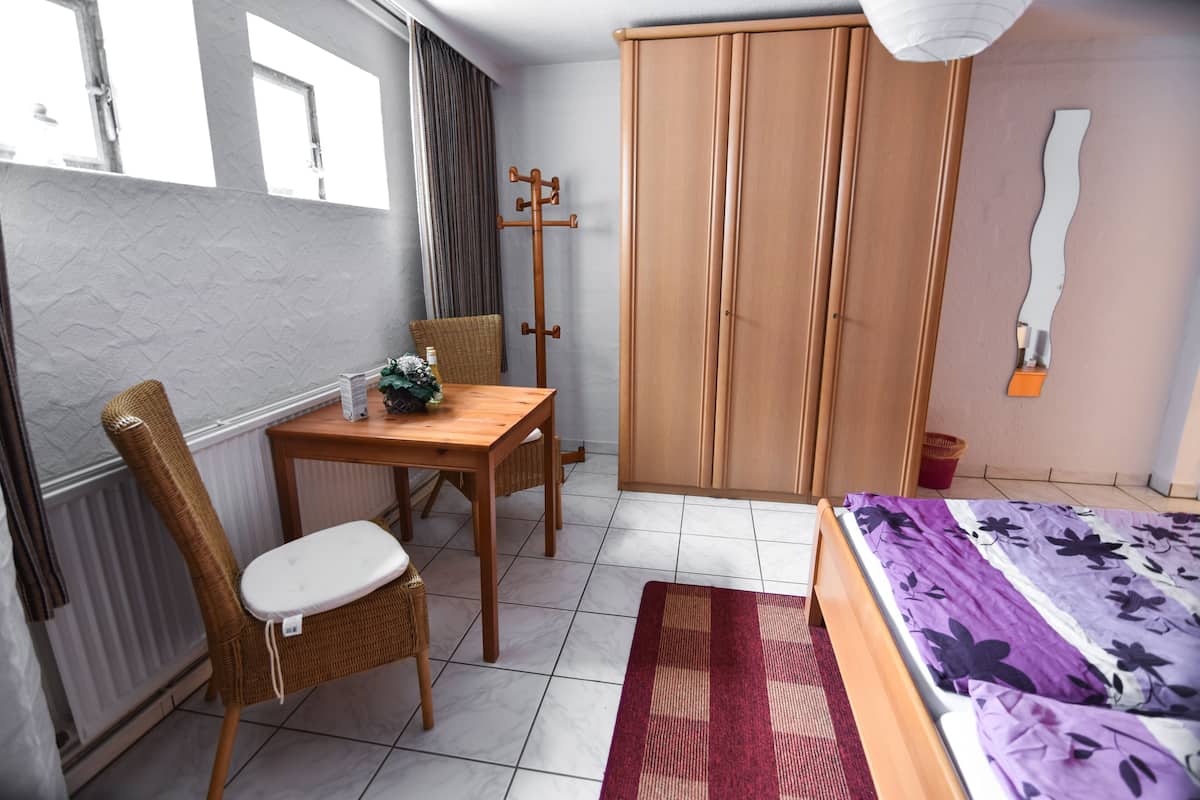 Ein Zimmer mit einem Bett, einem Holztisch mit Stuhl, einem Kleiderschrank und einer Heizung.