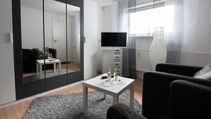 Ein modernes Wohnzimmer mit einem großen Spiegel, einem Flachbildfernseher, einem kleinen Tisch mit Flaschen und einem Sofa.
