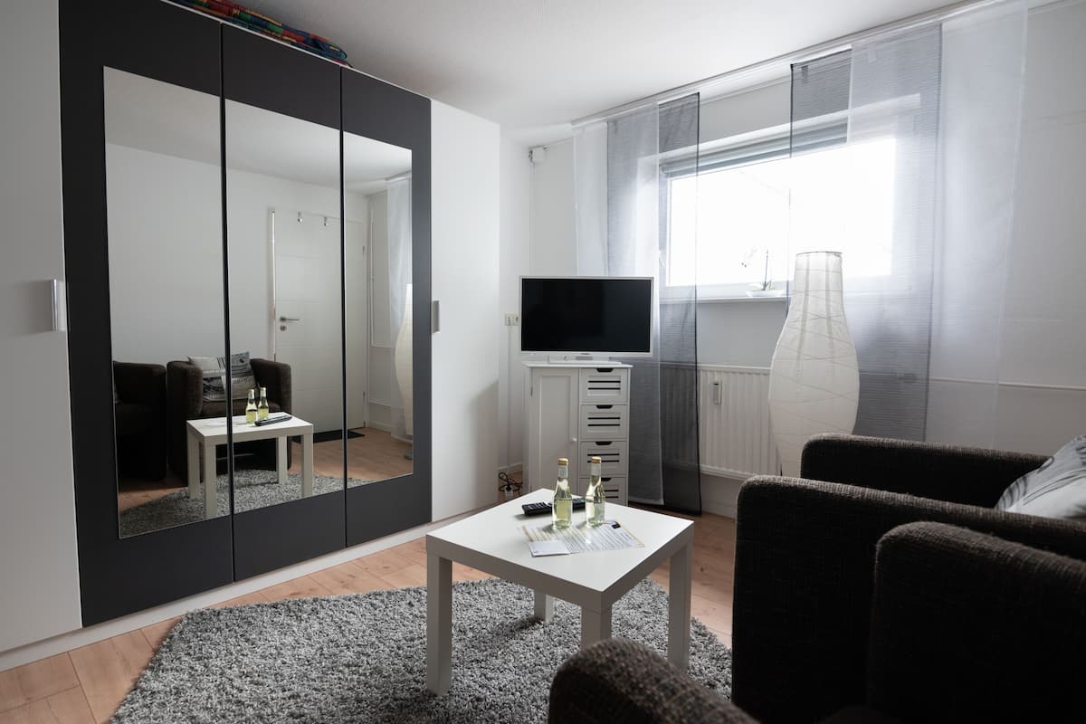Ein modernes Wohnzimmer mit einem großen Spiegel, einem Flachbildfernseher, einem kleinen Tisch mit Flaschen und einem Sofa.