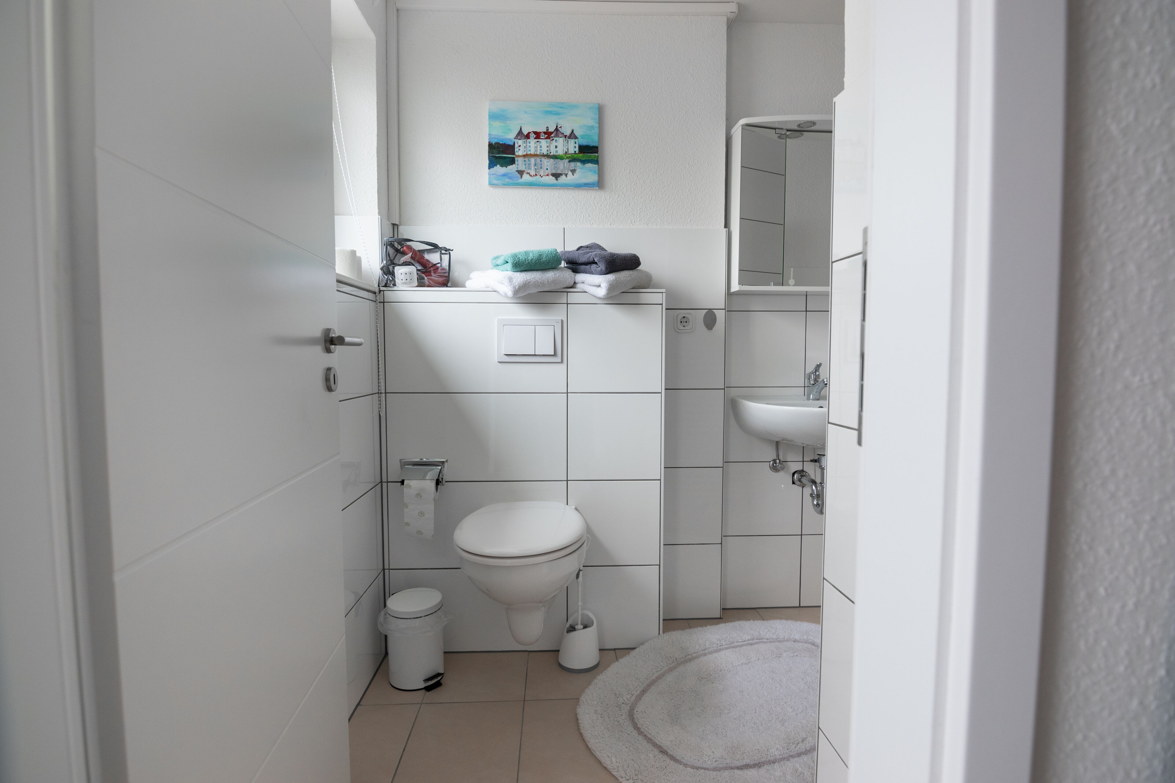 Un baño moderno con inodoro, lavamanos y un cuadro de un castillo en la pared.