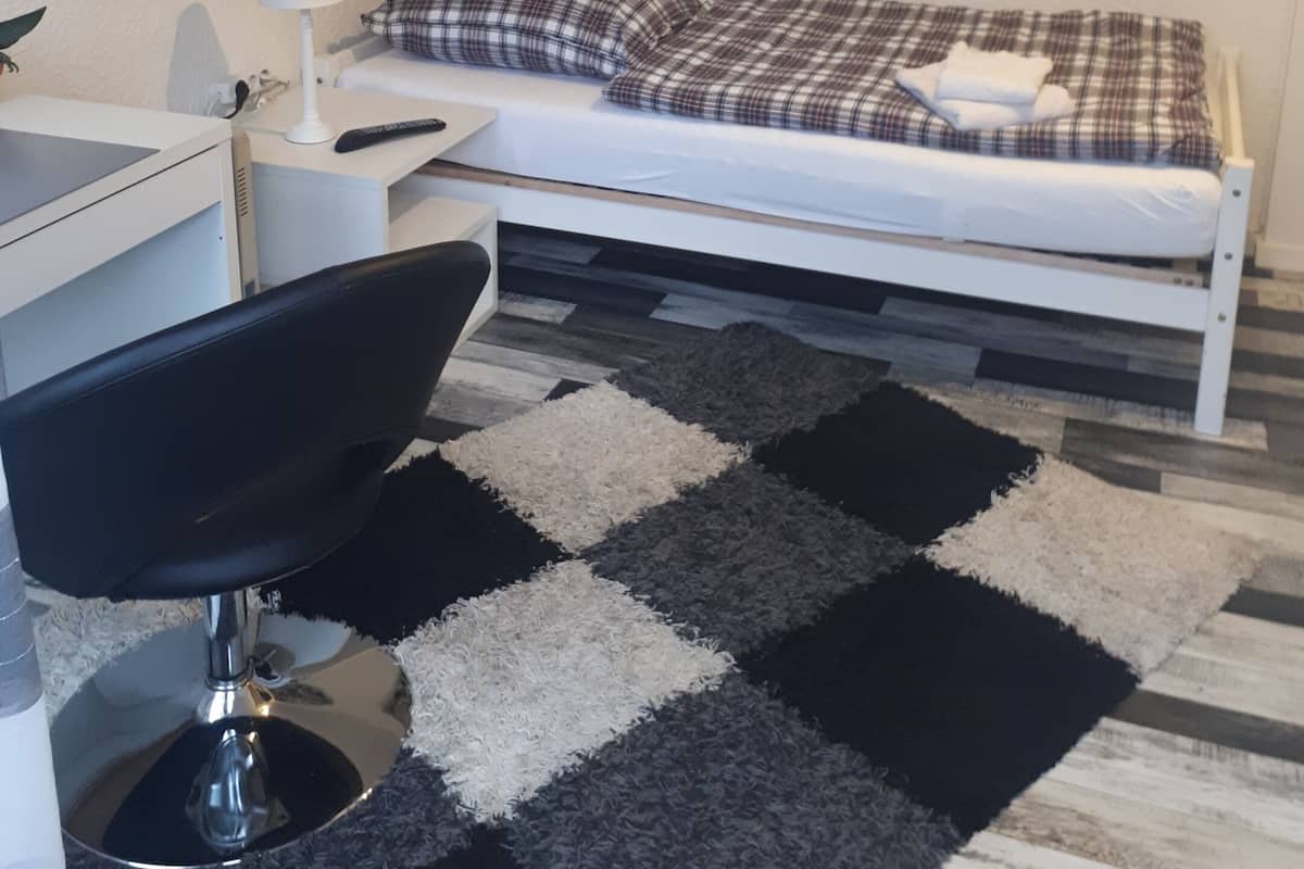 Ein Schlafzimmer mit einem Bett, einem Schreibtisch, einem Stuhl, einer Lampe und zwei Bildern an der Wand.