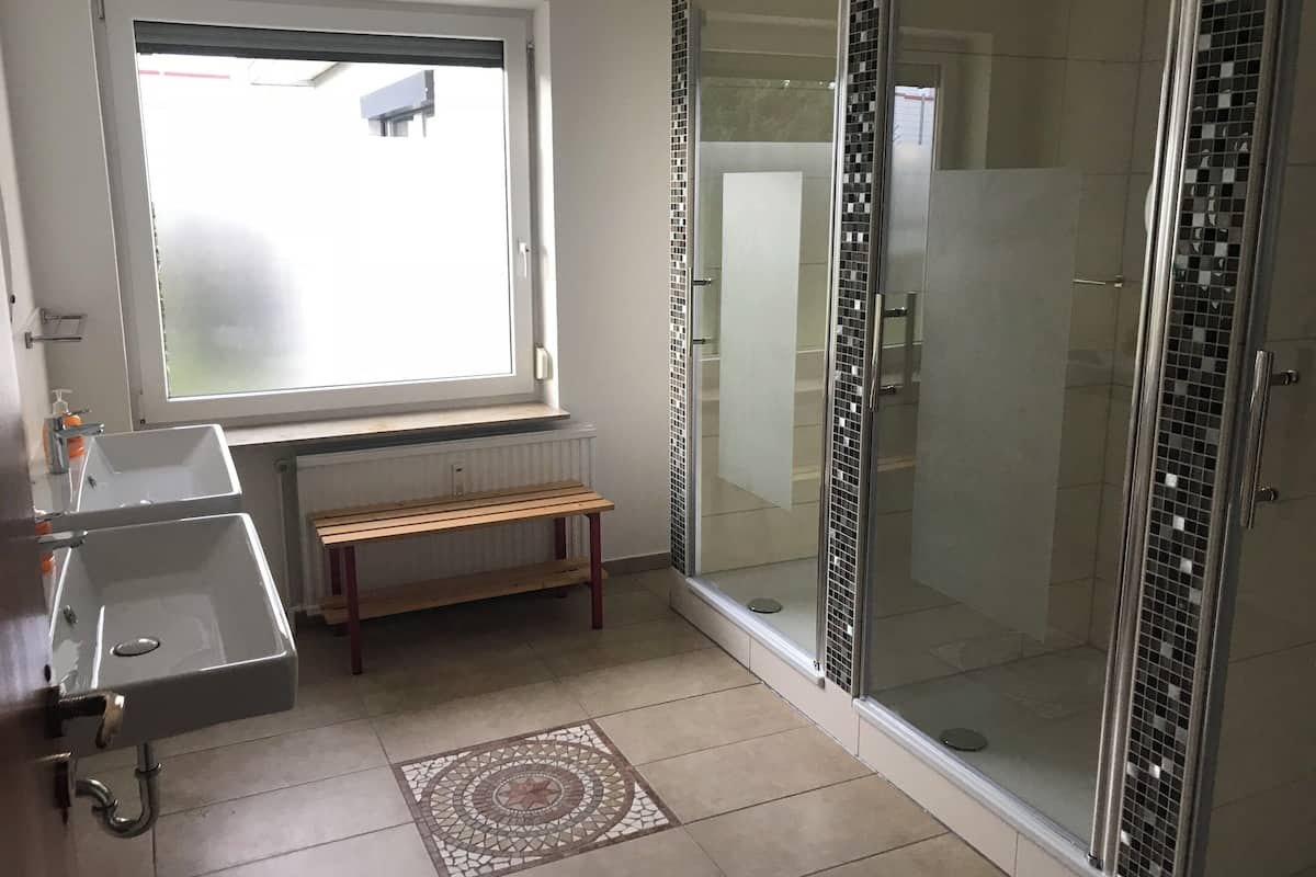 Ein Badezimmer mit Fenster, Waschbecken, Ablagefläche und Duschkabine aus Glas.
