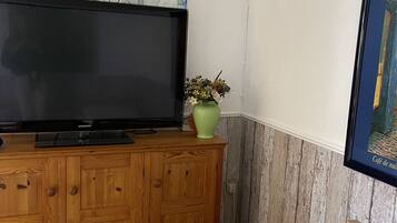 Ein Schlafzimmer mit einem Bett, einem Holzschrank mit Fernseher, einem grünen Blumenvasen und einem gerahmten Bild an der Wand.
