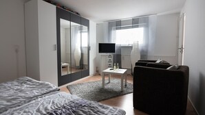 Ein modernes Hotelzimmer mit einem Bett, einer Couch, einem Fernseher, einem kleinen Tisch mit Flaschen und einem Kleiderschrank.