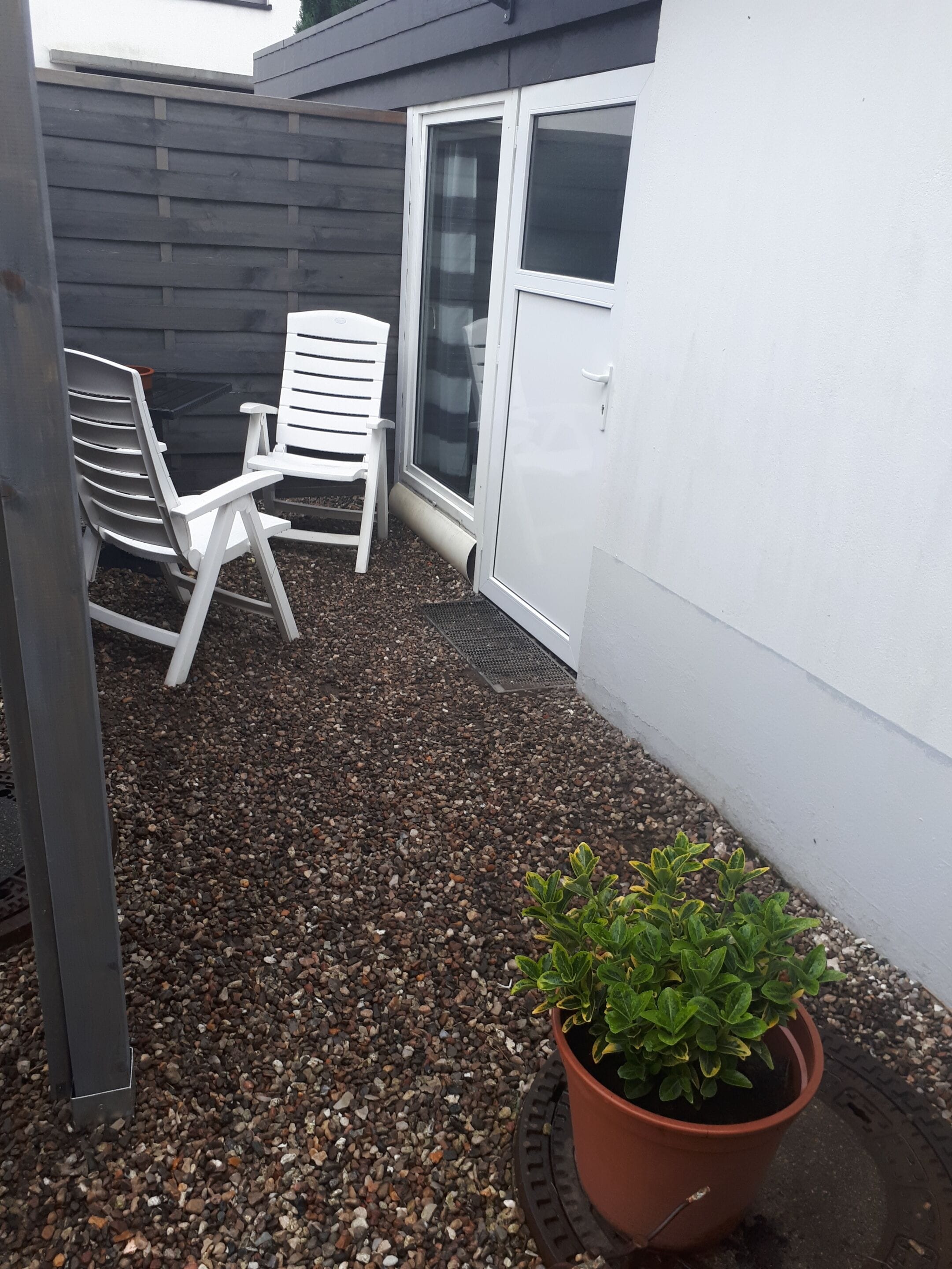 A patio area with a white chair, a potted plant, and a sliding glass door.