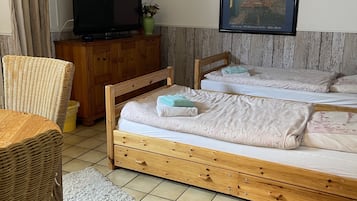 Ein Schlafzimmer mit zwei Holzbetten, einem Fernseher auf einem Holzschrank, einem Korbstuhl und einem Bild von Van Goghs 'Café Terrasse am Abend' an der Wand.