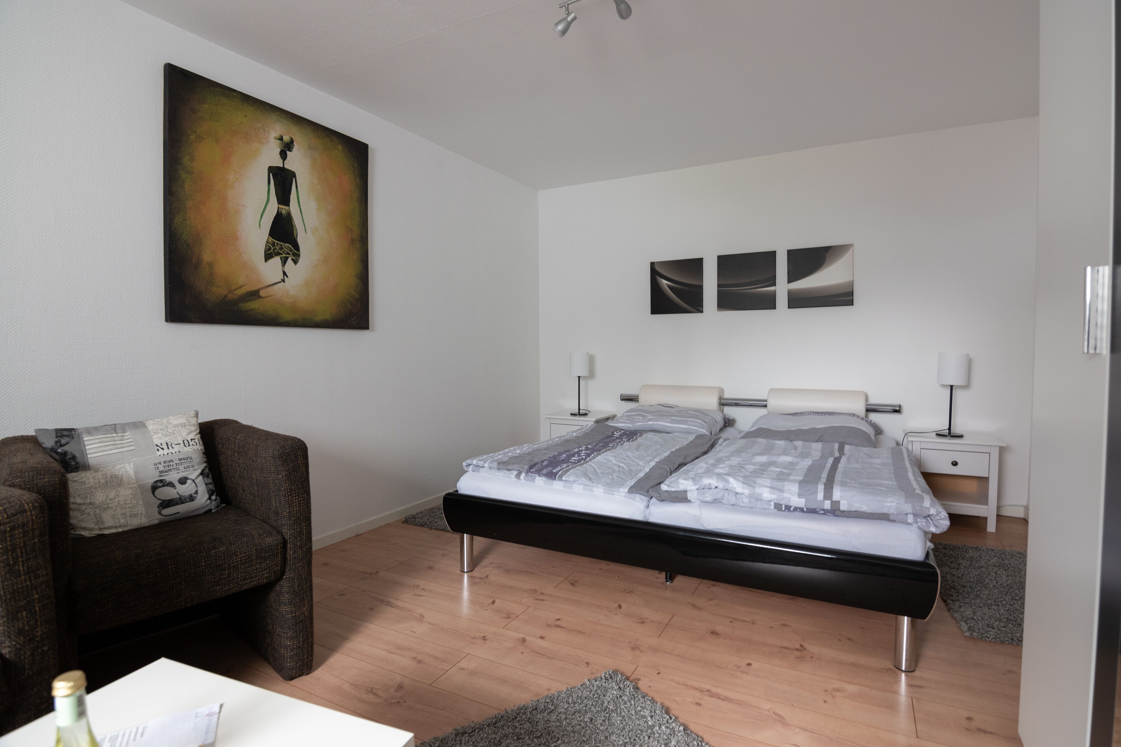 A modern bedroom with a bed, a sofa, a painting, and a nightstand.