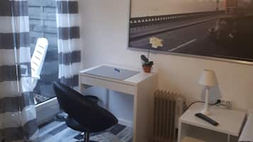 Ein kleines Hotelzimmer mit Bett, Schreibtisch, Stuhl, Heizkörper und einem fenster mit Vorhängen.