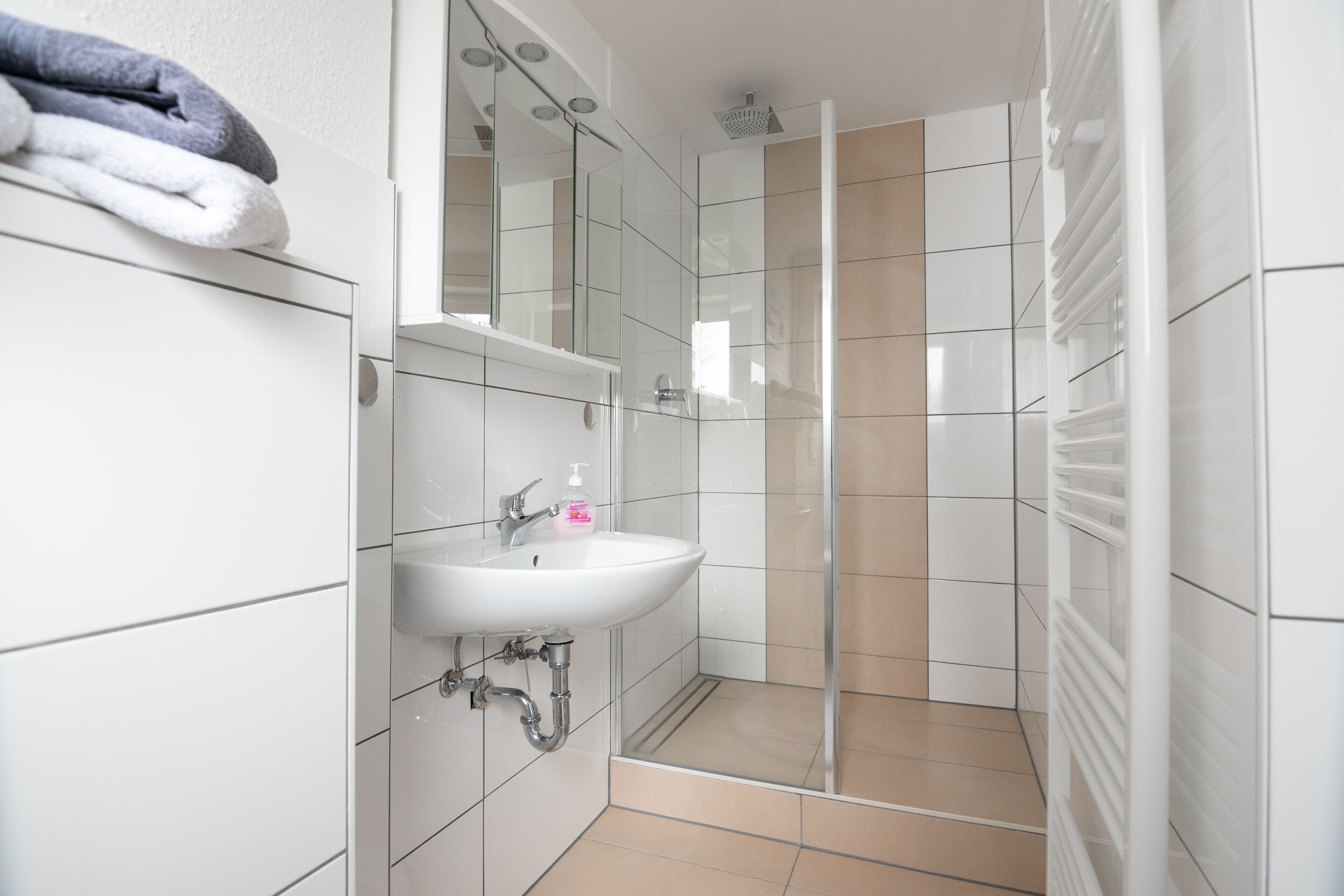 Un baño con lavamanos blanco, espejo y ducha.