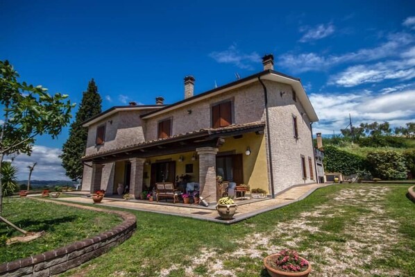 A two-story stone house with a covered porch, a stone wall surrounding the property, and a well-maintained lawn. - B&B dell'Aviatore (Narni)