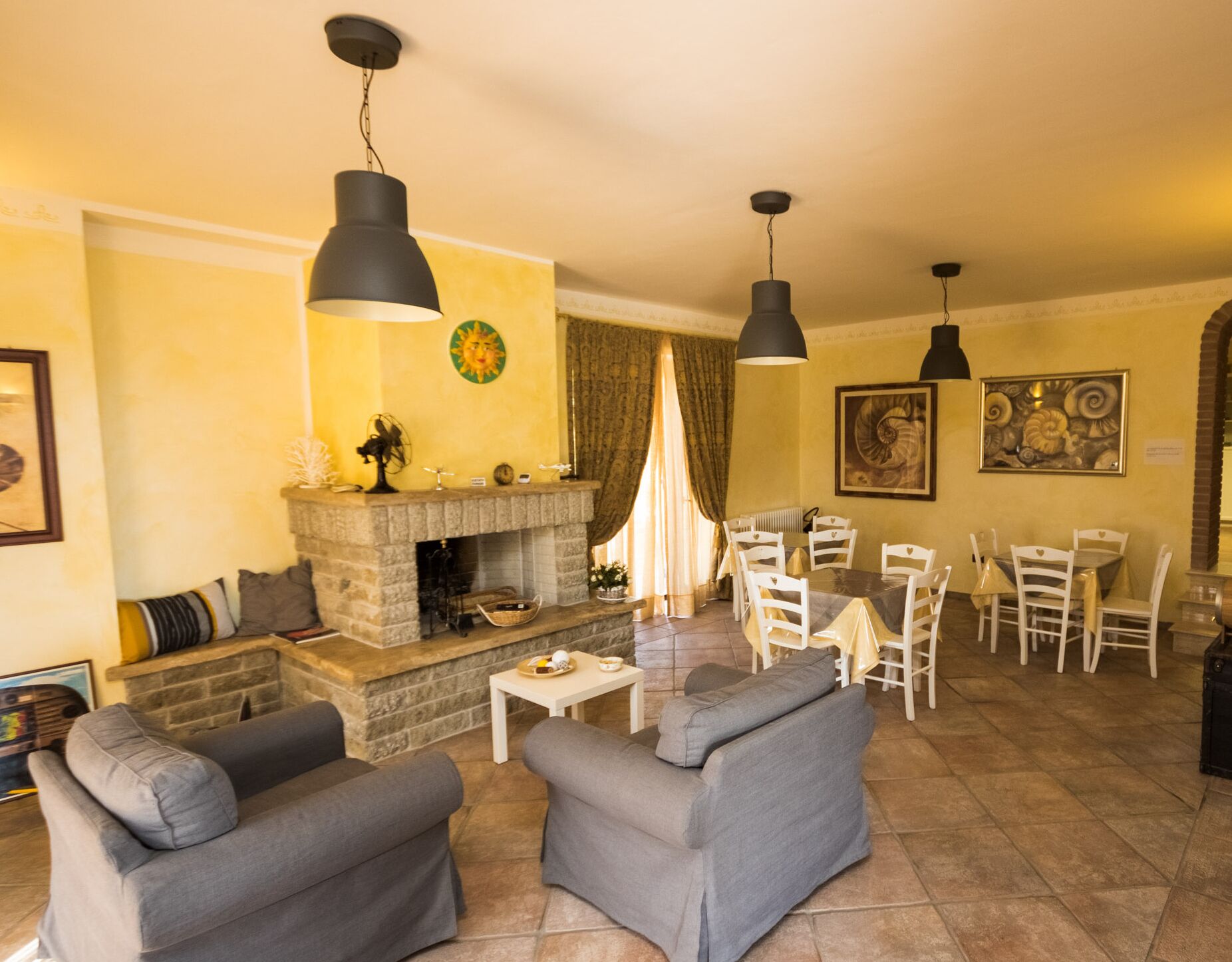 A living room with a fireplace, grey sofas, a dining area with white chairs, and pendant lighting.
