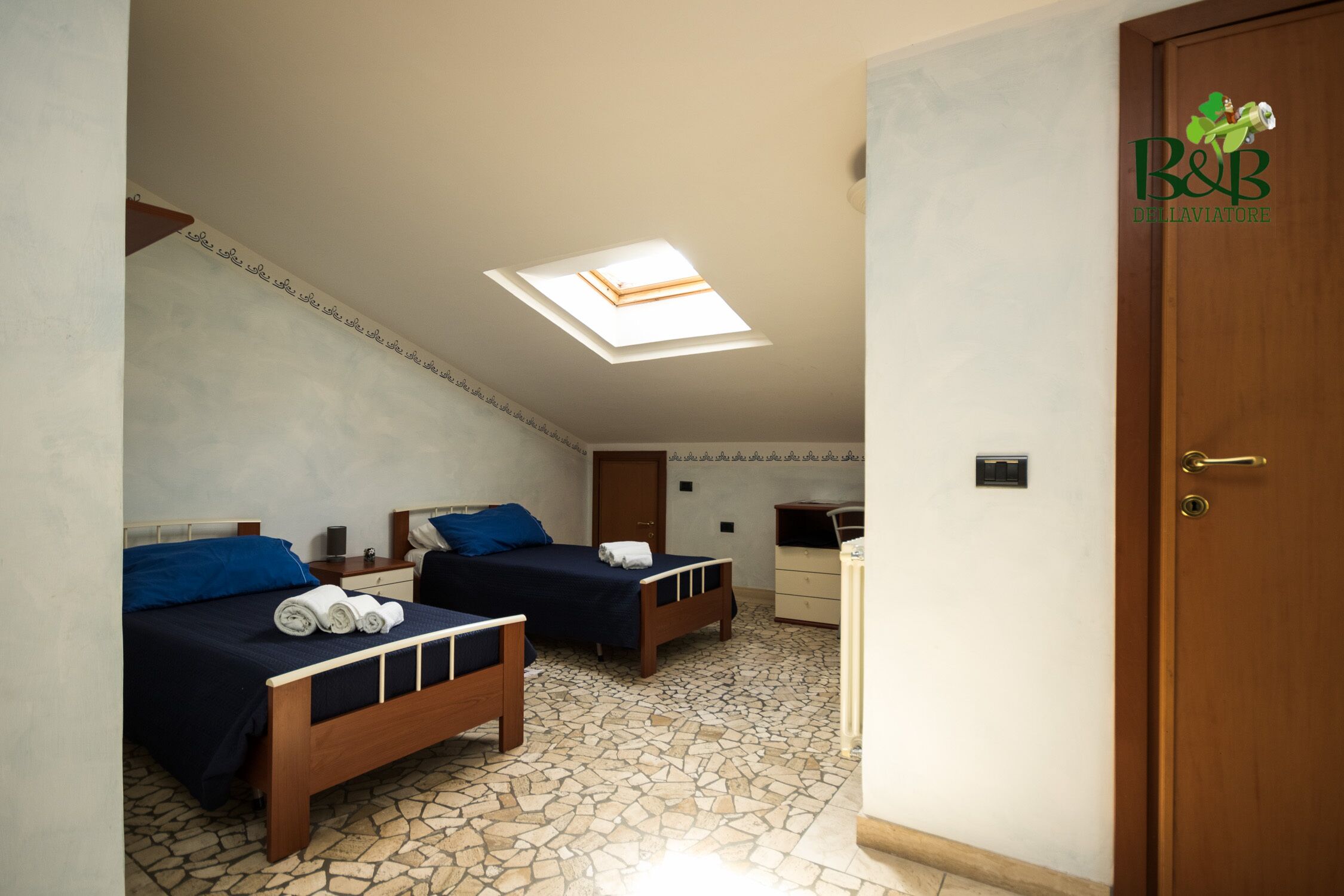 Een slaapkamer met twee bedden, een dakraam, een houten deur en een betegelde vloer.