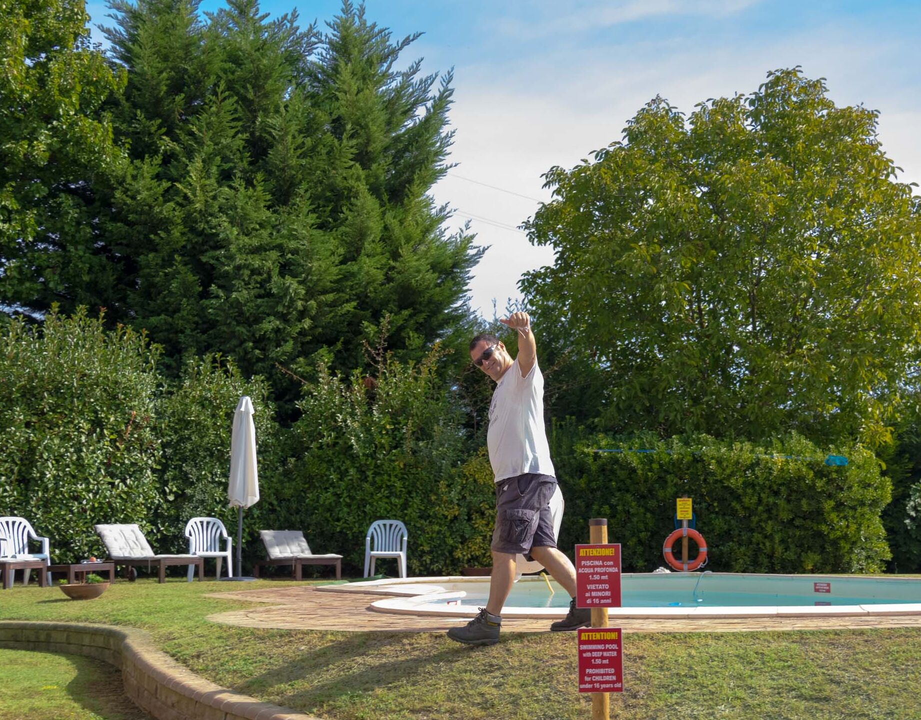 Un hombre juega con un disco volador cerca de una piscina con sillas de descanso y un letrero que indica una profundidad de 1,5 metros y una edad mínima de 16 años.