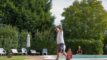 Ein Mann wirft Frisbee in der Nähe eines Schwimmbeckens mit Liegestühlen. Ein Schild weist auf eine Wassertiefe von 1,5 Metern und ein Mindestalter von 16 Jahren hin.