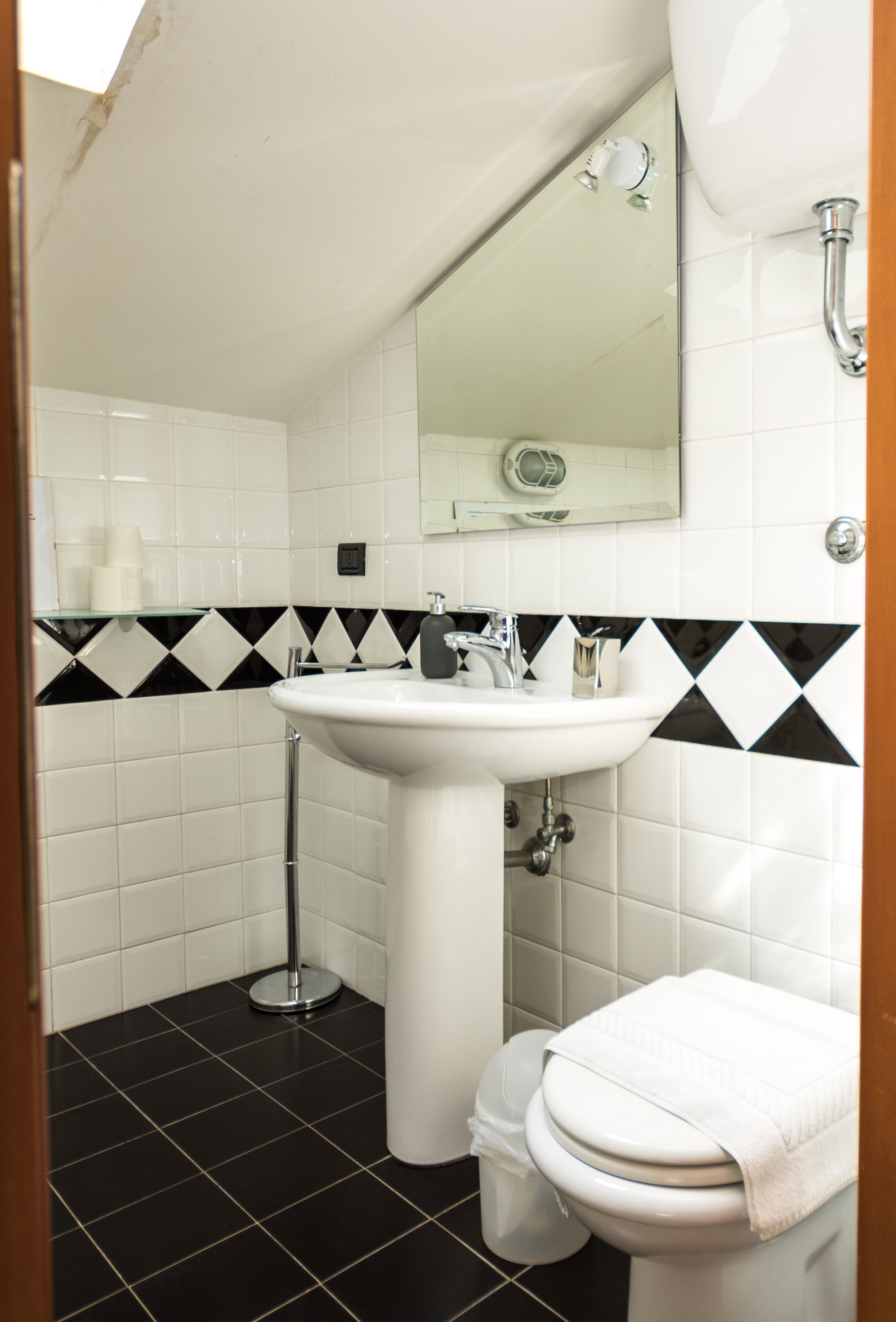 A bathroom with a white sink, black and white tiled walls, a mirror, and a toilet.