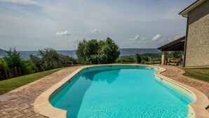 Une piscine rectangulaire à bord incurvé, entourée d’une terrasse en briques et d’une pelouse.