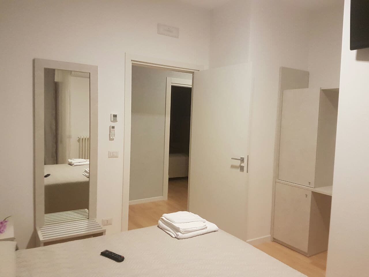 Una camera d'albergo con un letto, uno specchio, un armadio e una porta che dà su un'altra stanza.
