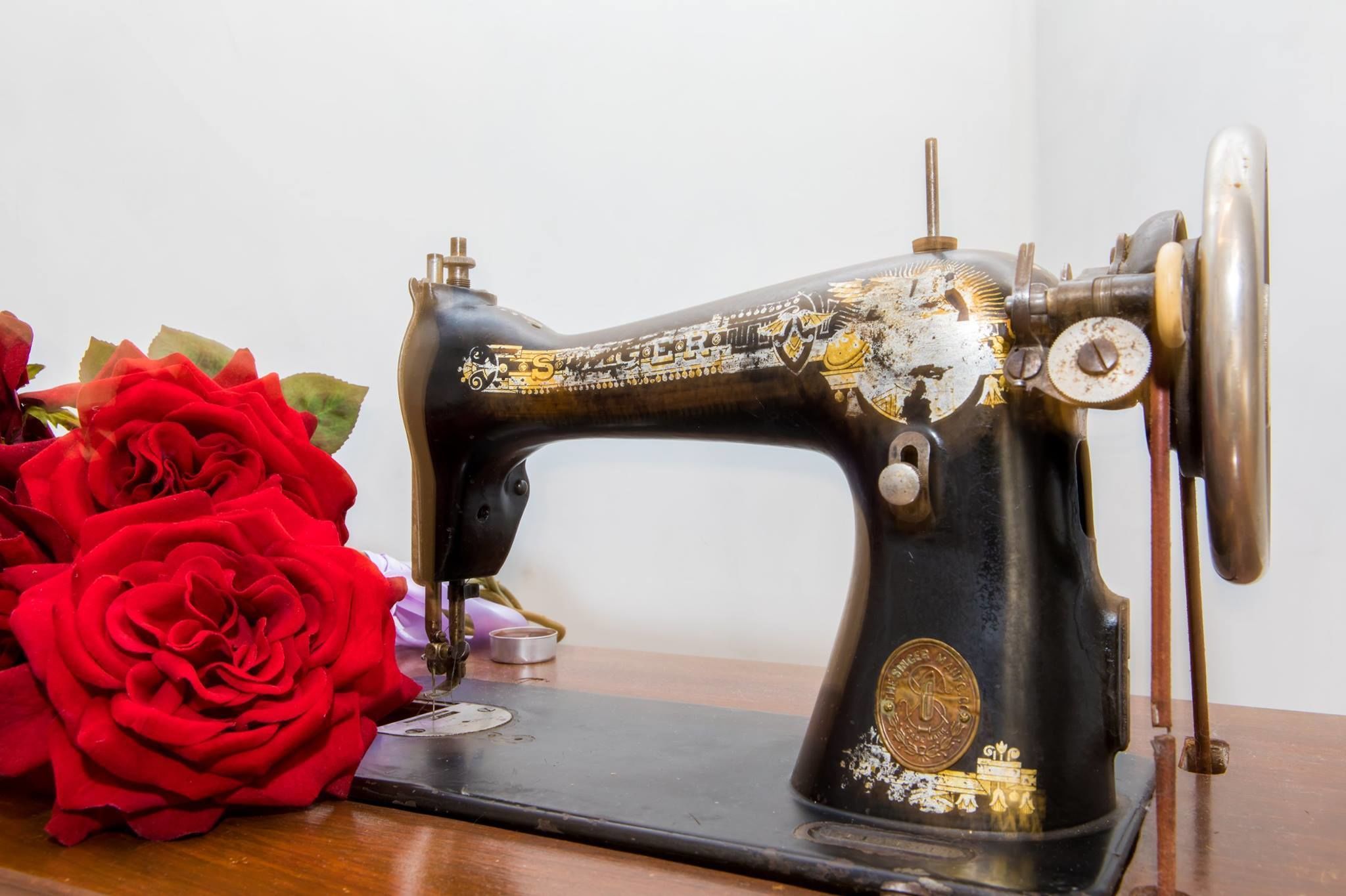Una máquina de coser antigua con un diseño decorativo, sobre una superficie de madera junto a un ramo de rosas rojas.