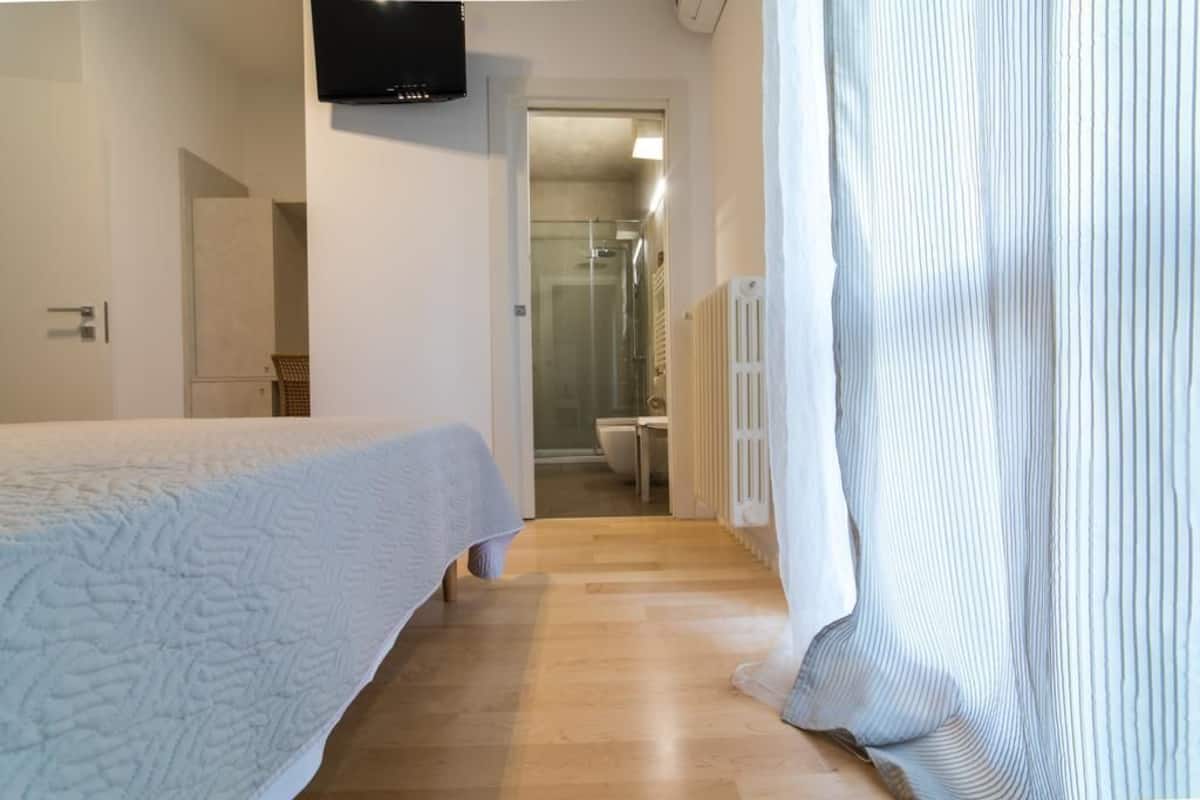 Ein Schlafzimmer mit Bett, Fernseher und angrenzendem Badezimmer, das durch eine geöffnete Tür sichtbar ist.