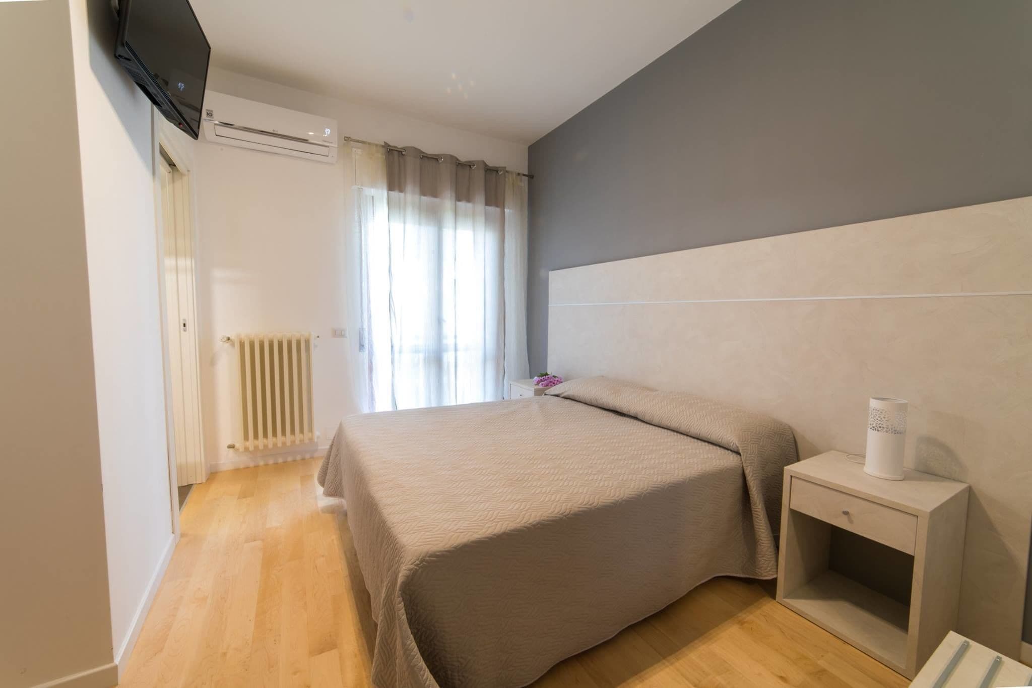 Un dormitorio con cama, mesita de noche, radiador y televisor montado en la pared.