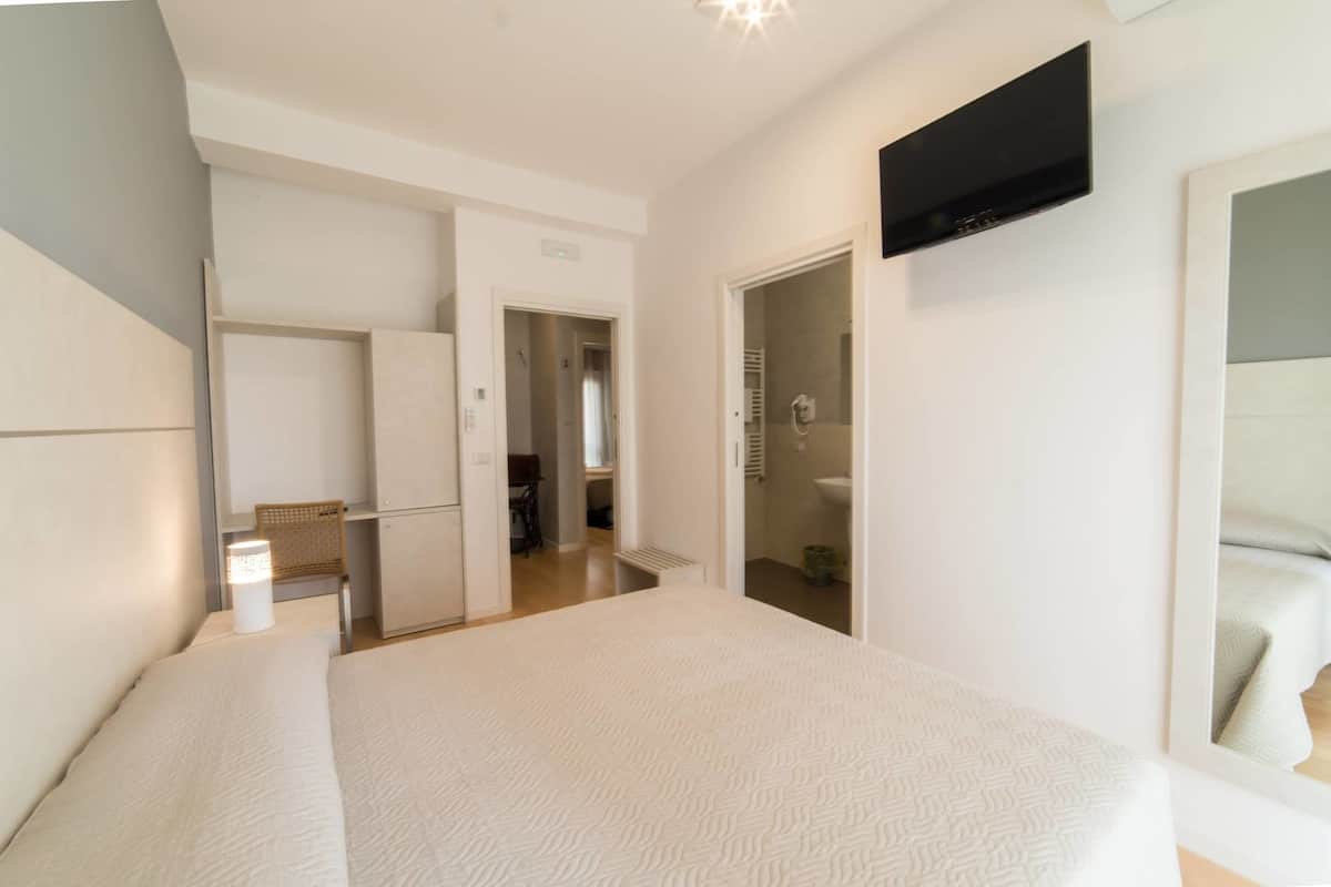 Ein modernes Schlafzimmer mit einem großen Bett, einem flachbildfernseher an der Wand und einem begehbaren Kleiderschrank.