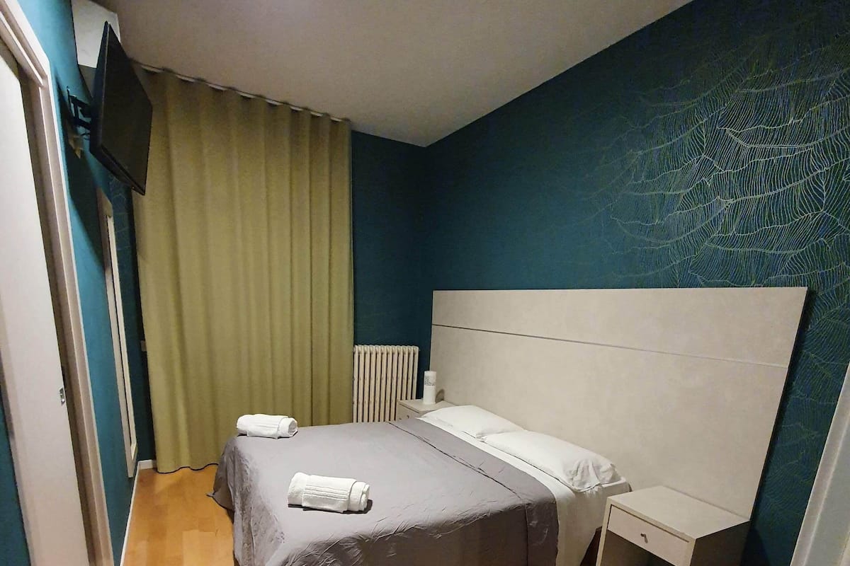 Ein Schlafzimmer mit einem Bett, einem Nachttisch und einem an der Wand befestigten Fernseher.