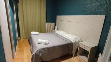 Quarto com cama, mesa de cabeceira e televisão fixada na parede.