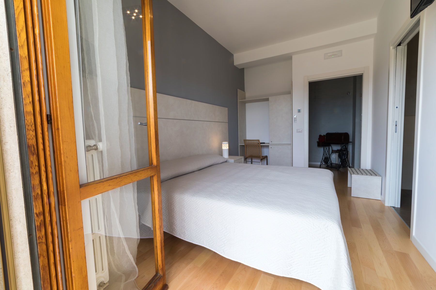 A bedroom with a large bed, a chair, a sewing machine, and a radiator.