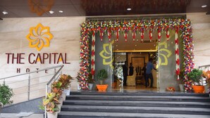 La entrada del Hotel The Capital, con fachada de mármol, un arco decorado con flores y una escalera que conduce a la entrada.