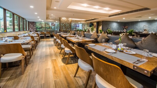 Un restaurante espacioso con largas mesas de madera y sillas acolchadas, ventanas amplias y un diseño de interiores moderno.