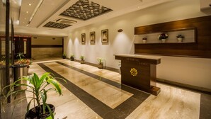Un hall de hotel con una recepción, plantas en macetas, obras de arte enmarcadas en las paredes y un techo con diseño.