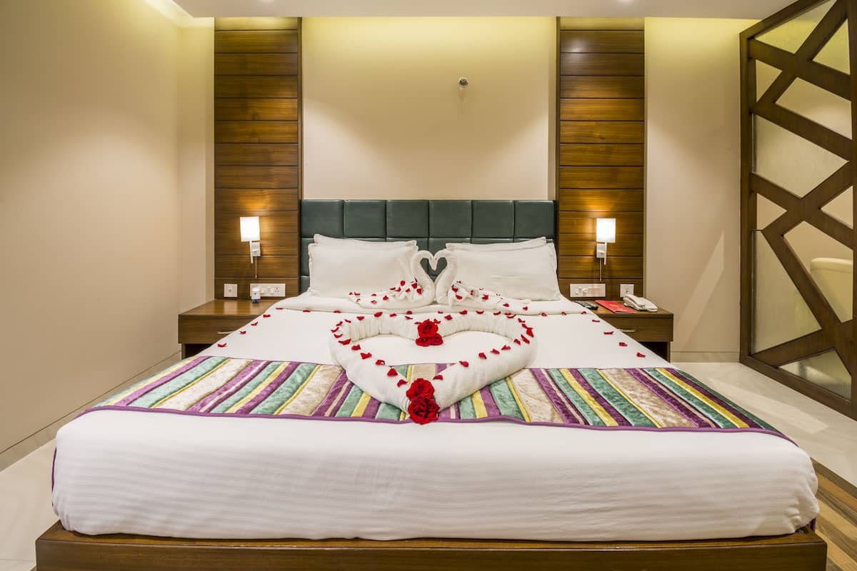 Habitación de hotel con una cama grande, cabecera de madera y un arreglo decorativo con forma de corazón sobre la cama.