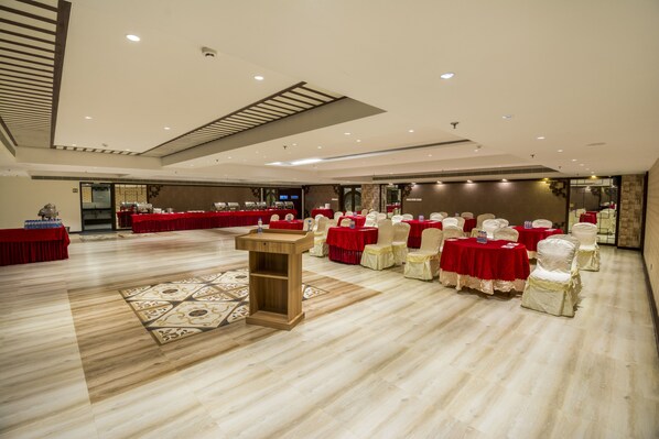 A spacious hall with multiple round tables covered in red tablecloths, arranged in rows. - The Capital Hotel (Guntur)