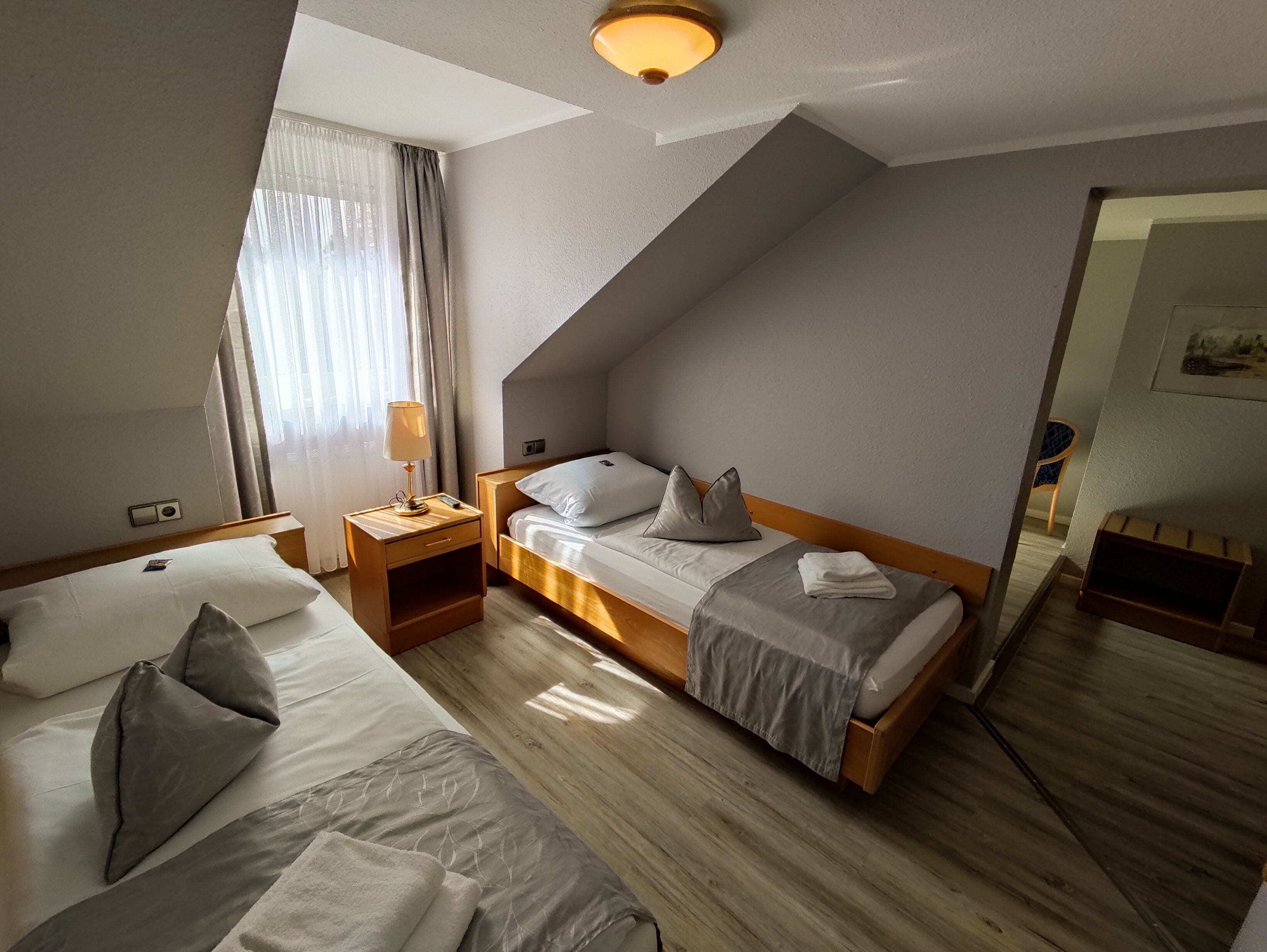 Ein Hotelzimmer mit zwei Betten, einem Nachttisch, einer Lampe und einem großen Spiegel.