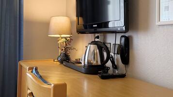 A hotel room with a wooden desk, a television, a lamp, a kettle, and a phone.