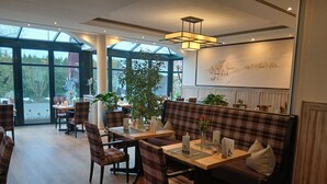 A restaurant with a wooden floor, plaid furniture, and large windows. - Hotel Zum Märchenwald (Lingen)