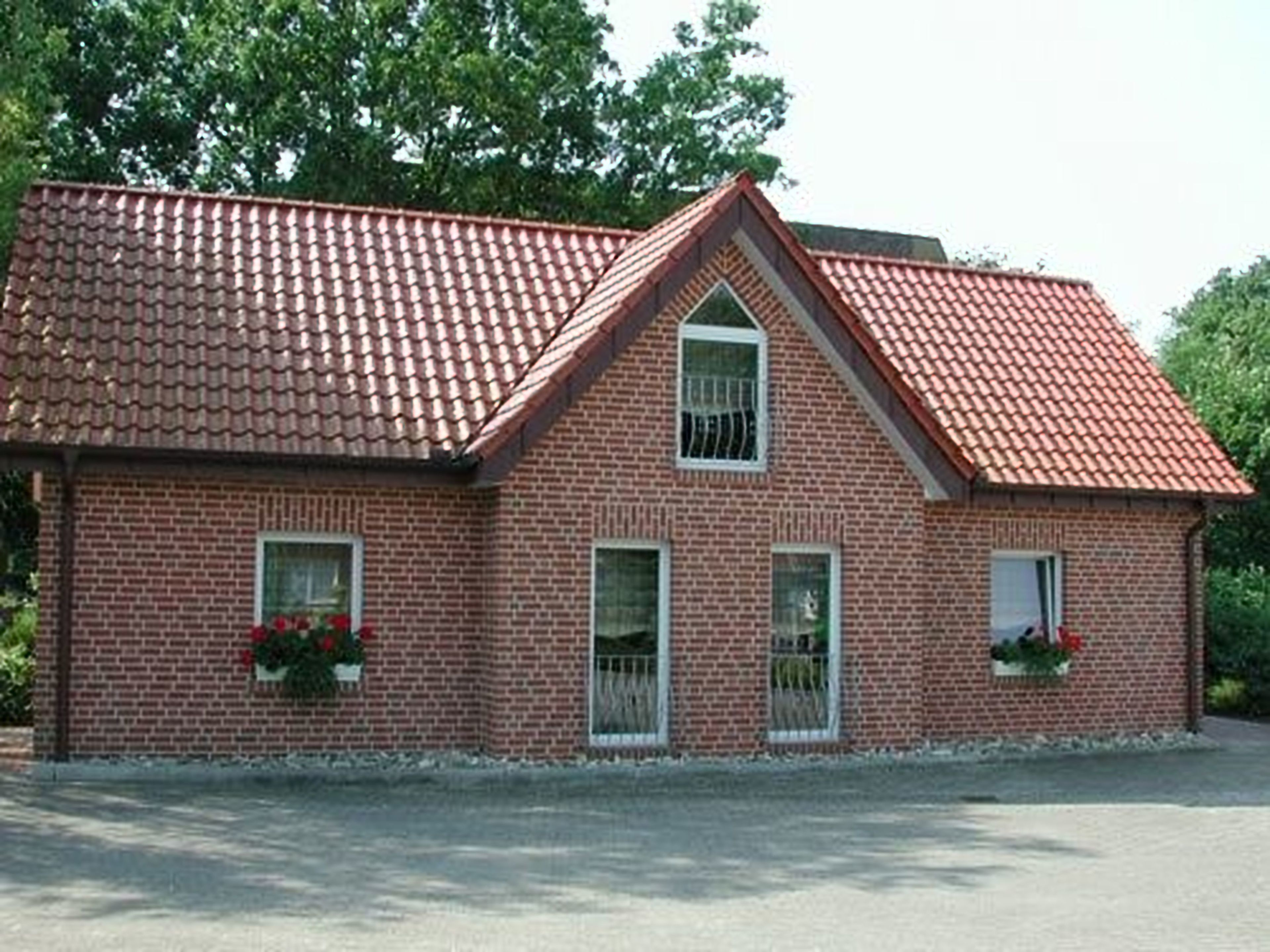 Et murstenshus med rødt tegltag, to vinduer med hvide rammer og blomsterkasser i stueetagen.