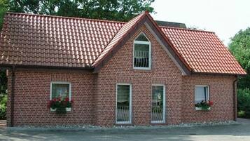 Et murstenshus med rødt tegltag, to vinduer med hvide rammer og blomsterkasser i stueetagen.