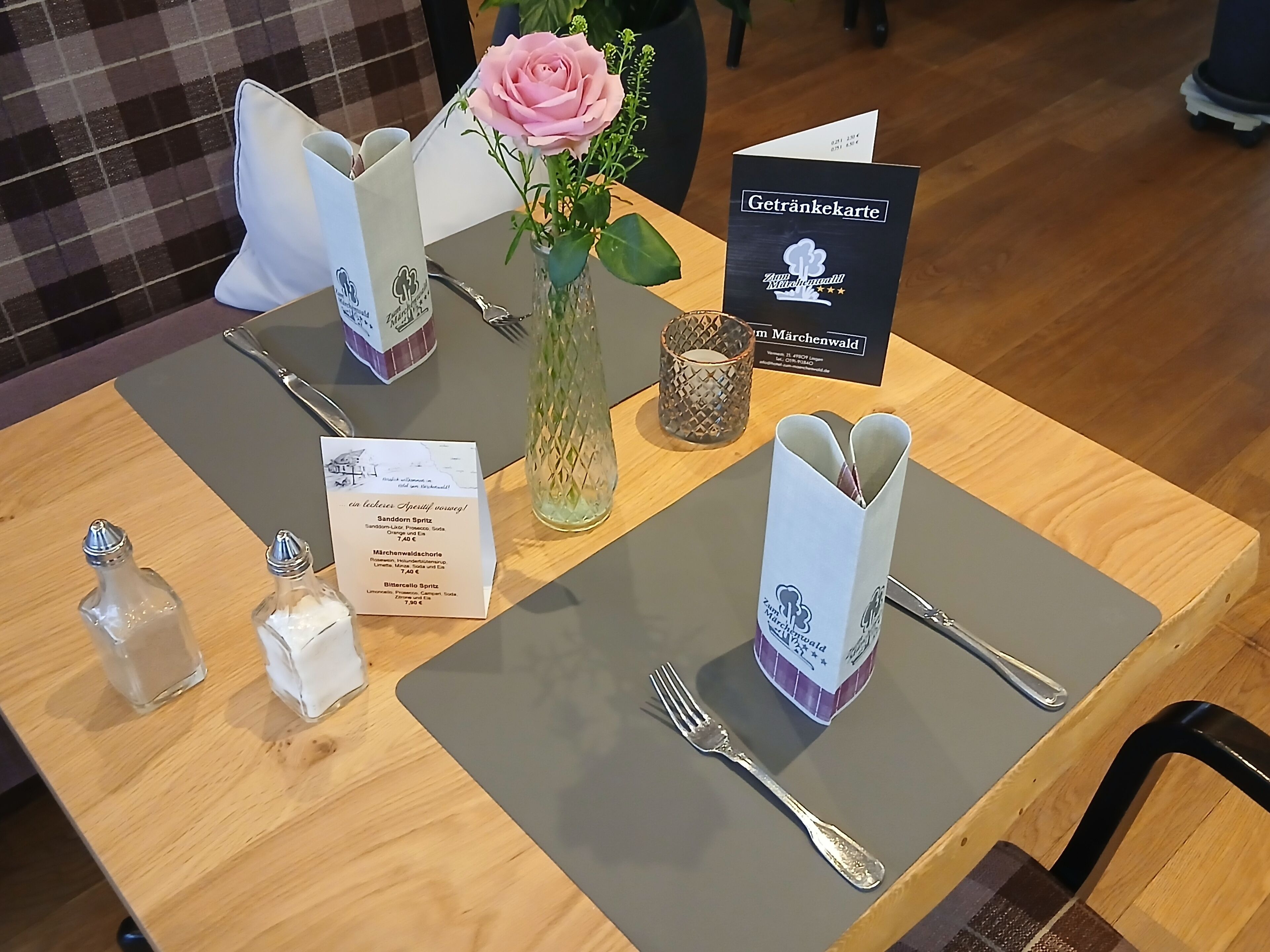 Una mesa dispuesta con un menú, un florero con una rosa rosa, saleros y pimenteros, y una tarjeta con el texto 
