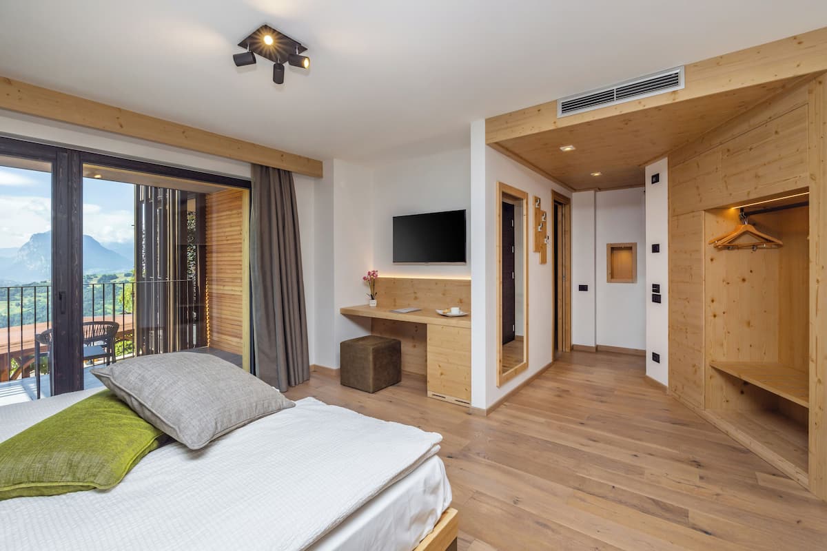 A modern hotel room with a large bed, a desk, a TV, and a balcony with a mountain view.