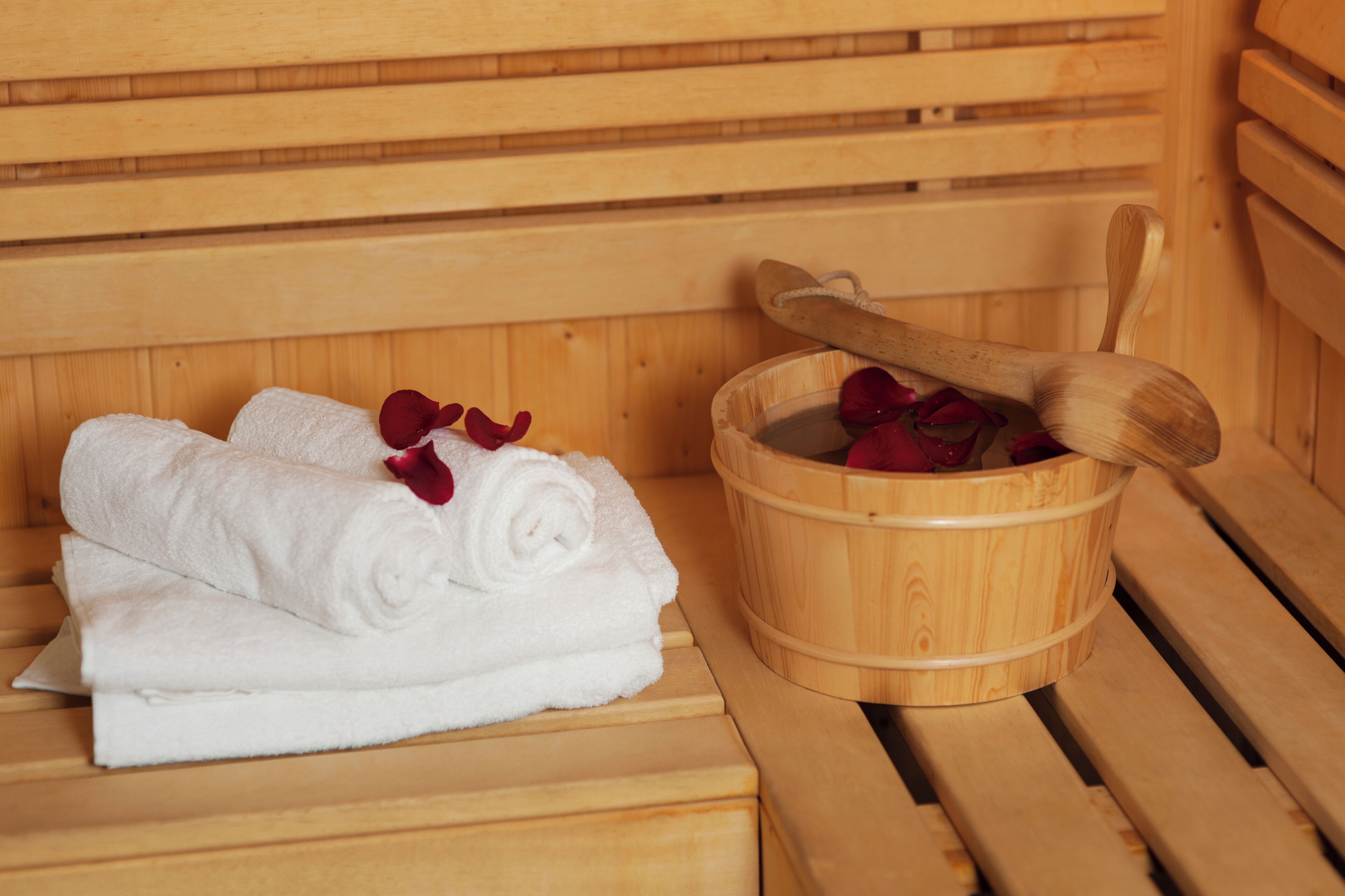 Banca de sauna de madera con un cubo de madera que contiene un mortero de madera y pétalos de rosa roja.