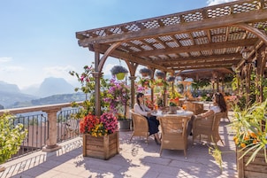A terrace with wicker furniture, potted plants, and a view of mountains.